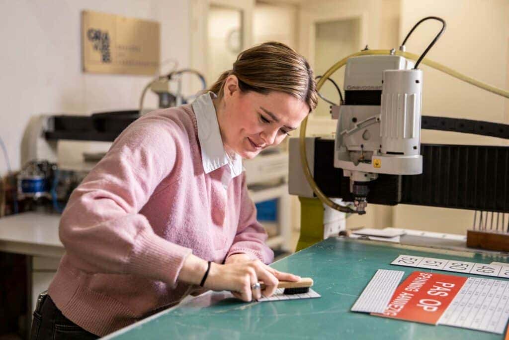 Medewerkster van Gravure85 maakt gefreesde kunststof plaatjes schoon